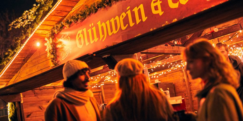 Das Bild zeigt drei Personen vor einem Stand auf dem Weihnachtsmarkt in Dortmund